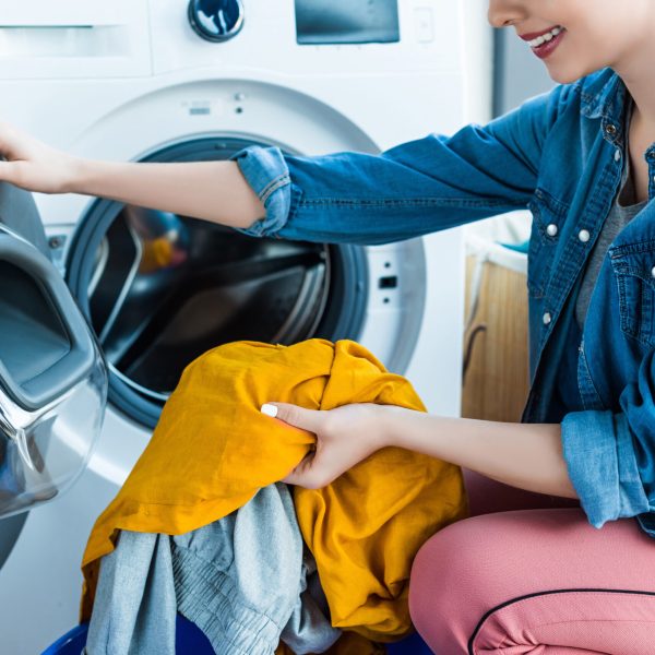 cropped shot of smiling young woman taking laundry from washing machine